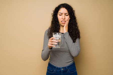 Photo for Upset young woman drinking cold ice water and suffering from teeth sensitivity or dental pain - Royalty Free Image