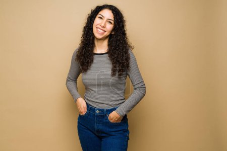 Photo for Beautiful hispanic woman in her 20s smiling with her hands in the pockets wearing casual clothes - Royalty Free Image