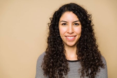 Foto de Attractive young woman with curly hair smiling and looking at the camera against a studio background - Imagen libre de derechos