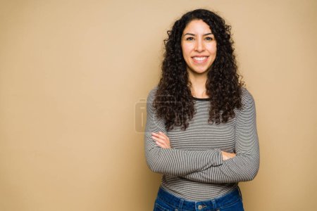 Foto de Gorgeous latin young woman with curly hair wearing casual clothes smiling with her arms crossed - Imagen libre de derechos