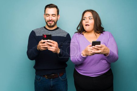 Téléchargez les photos : Shocked fat woman spying on his cheating happy boyfriend while texting another woman on the smartphone - en image libre de droit