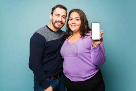 Foto de Beautiful young couple making eye contact smiling and showing the smartphone screen while using social media - Imagen libre de derechos