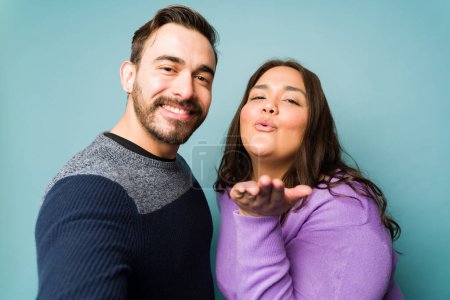 Foto de Attractive romantic couple dating and blowing a kiss while taking a selfie together for social media - Imagen libre de derechos