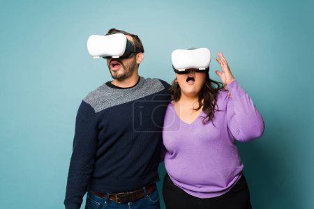 Foto de Surprised young couple using VR glasses and looking shocked while playing with virtual reality technology - Imagen libre de derechos