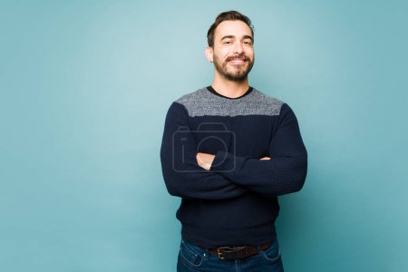 Photo for Handsome caucasian man in his 30s smiling looking happy with his arms crossed against a blue studio background - Royalty Free Image