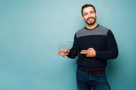 Téléchargez les photos : Excited attractive young man pointing two fingers to copy space ad and smiling in front of a studio background - en image libre de droit