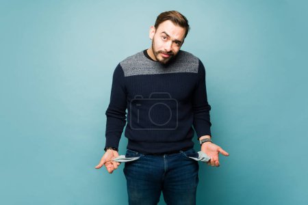 Photo for Broke stressed man with no money emptying his pockets and feeling poor against a studio background - Royalty Free Image