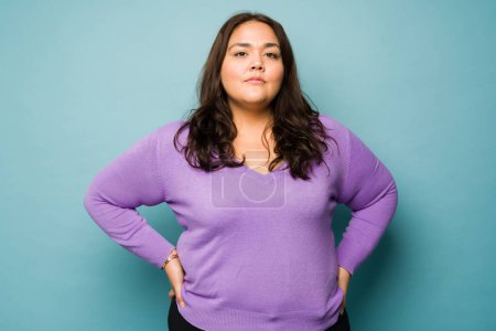 Téléchargez les photos : Serious overweight hispanic woman with her hands on the hips looking determined while making eye contact - en image libre de droit