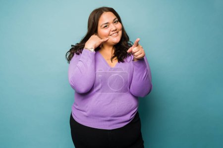 Téléchargez les photos : Mexican obese young woman smiling making a phone gesture and asking to make a call while pointing - en image libre de droit