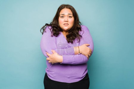 Photo for Upset latin overweight woman feeling cold and shivering looking sad against a studio background - Royalty Free Image