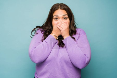 Foto de Shocked fat young woman covering her mouth and looking sick suffering from bad breath - Imagen libre de derechos