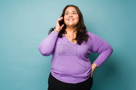 Photo for Excited obese young woman making a call and talking on the phone with family or friends and smiling - Royalty Free Image