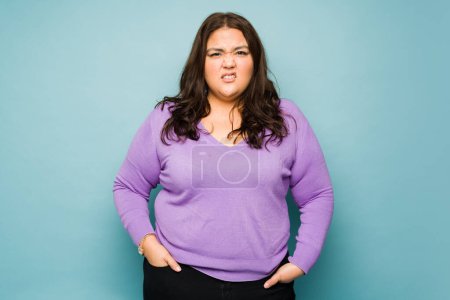 Photo for Sick obese young woman feeling ill and nauseous while looking frustrated in front of a studio background - Royalty Free Image