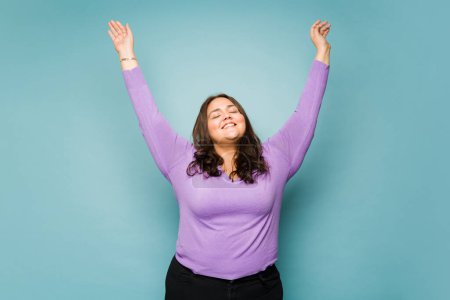 Photo for Carefree fat young woman looking happy dancing raising her arms looking relaxed and cheerful - Royalty Free Image