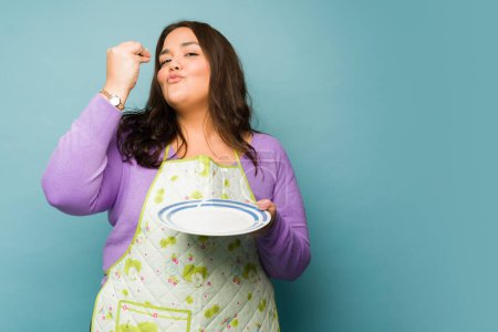 Photo for Happy young woman doing a chef's kiss after finishing eating delicious food after cooking - Royalty Free Image