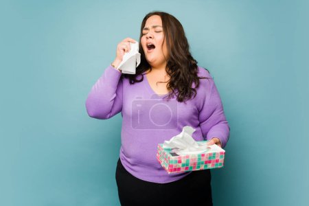 Foto de Sick obese latin woman sneezing feeling ill with a cold or flu while using tissues - Imagen libre de derechos