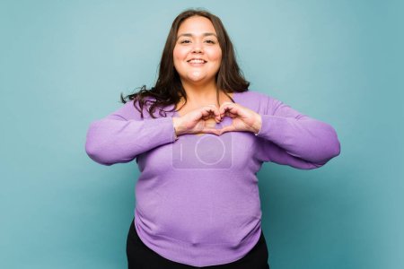 Photo for Portrait of a happy fat woman making a heart gesture with her hands and putting in her chest feeling in love - Royalty Free Image