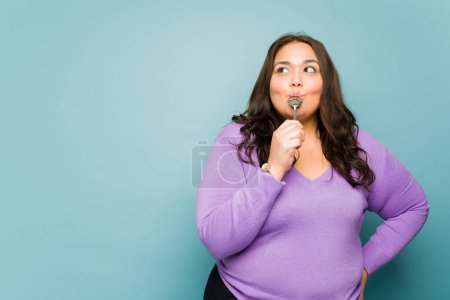 Photo for Beautiful latin fat woman eating delicious dessert with a spoon looking very happy - Royalty Free Image