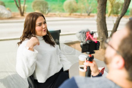 Téléchargez les photos : Hispanic chubby latin woman talking to the camera and filming social media content while drinking coffee with her boyfriend - en image libre de droit