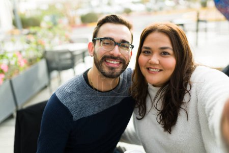 Photo for Personal perspective of a handsome caucasian boyfriend and fat girlfriend looking happy taking a selfie together at a restaurant - Royalty Free Image