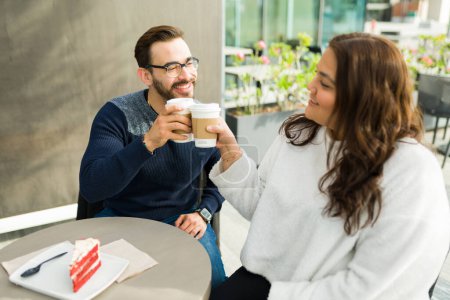 Téléchargez les photos : Happy boyfriend and big girlfriend making a toast with coffee while on a date at a cafe and eating a dessert - en image libre de droit