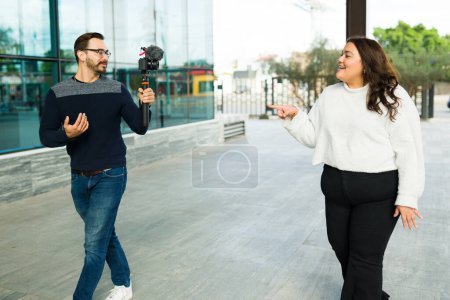 Foto de Caucasian man filming a woman influencer making video blogs and content for her social media in the city - Imagen libre de derechos