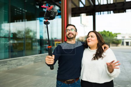 Foto de Happy influencer couple making video blogs and content for social media while filming with a camera outdoors in the city - Imagen libre de derechos