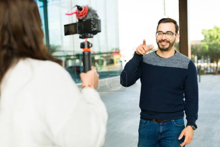 Téléchargez les photos : Rear view of a woman filming a happy caucasian man influencer creating content for social media - en image libre de droit