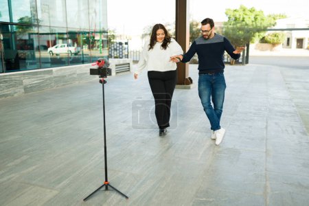 Photo for Fun influencer couple dancing with music outdoors in the city while making content for their social media - Royalty Free Image