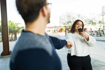 Photo for Hispanic fat woman taking a picture with her smartphone for social media while holding hands with her boyfriend during a date - Royalty Free Image