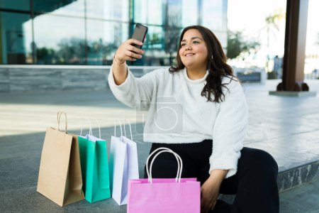 Foto de Beautiful chubby latin woman and content creator taking a selfie with her shopping bags for her social media followers - Imagen libre de derechos