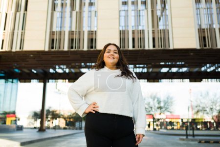 Photo for Attractive hispanic fat woman looking powerful while smiling and making eye contact while posing outdoors in the city - Royalty Free Image