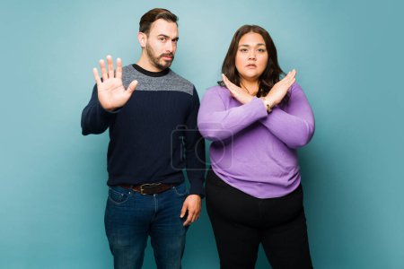 Téléchargez les photos : Upset angry young couple looking annoyed while making a stop gesture and against violence or discrimination - en image libre de droit