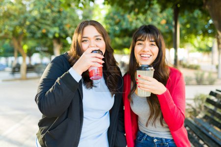 Téléchargez les photos : Portrait of attractive cheerful best friends drinking coffee and enjoying a walk in the park together - en image libre de droit