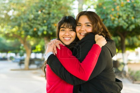 Photo for Happy latin women friends sharing love and hugging while smiling and making eye contact outdoors - Royalty Free Image