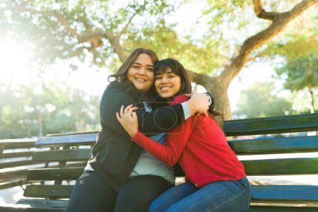 Téléchargez les photos : Happy young women friends with a beautiful loving friendship embracing while hanging out at the park - en image libre de droit