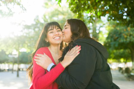 Photo for Attractive hispanic women friends with a beautiful friendship giving a kiss and making eye contact - Royalty Free Image