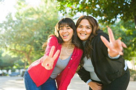 Foto de Excited young women friends making the peace sign while having fun together outdoors - Imagen libre de derechos