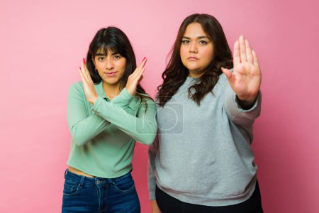 Foto de Upset hispanic young women looking angry while making showing their palm making a stop gesture - Imagen libre de derechos