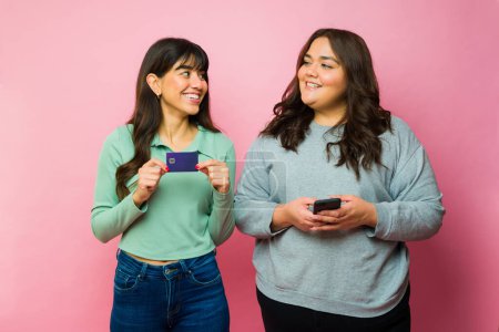 Photo for Happy women best friends showing a credit card while online shopping and using the smartphone - Royalty Free Image