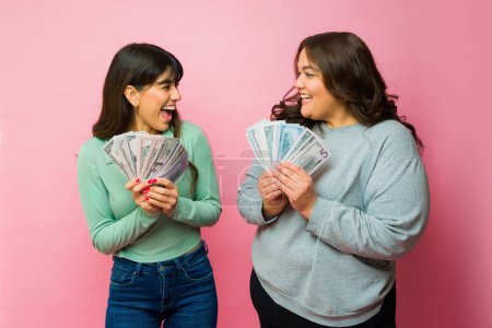 Téléchargez les photos : Excited women best friends feeling rich while showing a lot of money and screaming with happiness - en image libre de droit