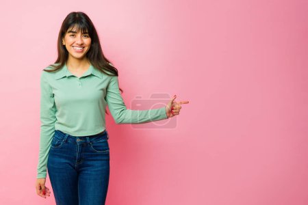 Téléchargez les photos : Gorgeous hispanic young woman smiling and pointing to a copy space ad against a pink background - en image libre de droit