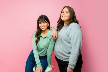 Photo for Beautiful young women best friends posing together and smiling in front of a pink background - Royalty Free Image