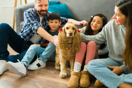 Photo for Smiling pet lover family with kids petting their adorable golden cocker spaniel dog while spending time together at home - Royalty Free Image