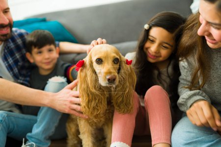 Téléchargez les photos : Excited family and kids petting their adorable golden cocker spaniel dog looking happy while having a good time at home - en image libre de droit