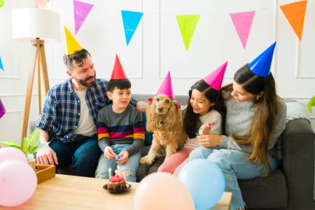 Foto de Beautiful family with children celebrating their cute pet's birthday party with a cake and party hats - Imagen libre de derechos