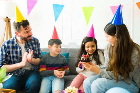 Téléchargez les photos : Cheerful young girl with her parents and sibling making a birthday wish with a cake during her home party - en image libre de droit