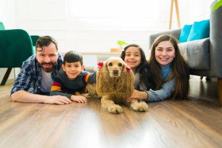 Photo for Cheerful family with young kids smiling relaxing in the living room with their beautiful cocker spaniel dog - Royalty Free Image