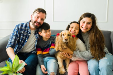 Téléchargez les photos : Beautiful happy family with children hugging and resting on the sofa while petting their adorable cocker spaniel dog - en image libre de droit