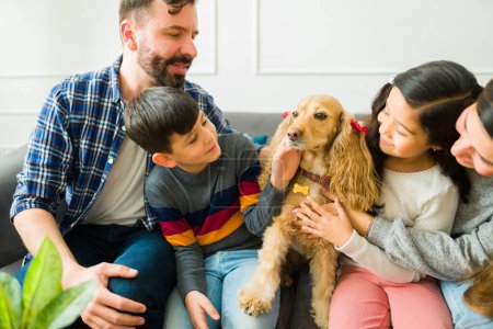 Photo for Happy family playing and petting their adorable cocker spaniel dog while relaxing together at home - Royalty Free Image